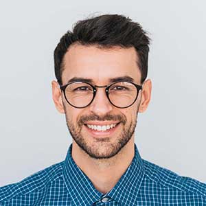 A smiling person wearing glasses, from the top of the head to the top of the shoulders.