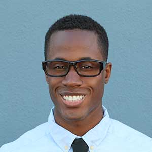 A smiling man wearing glasses, from the top of his head to the top of his shoulders.