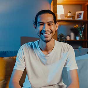 A person from the top of the head down to the waist, sitting in a cluttered bedroom.